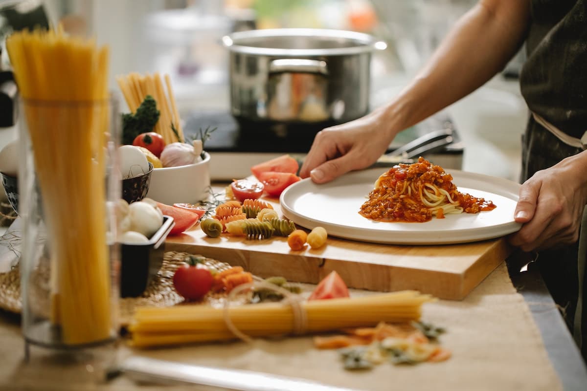 Chef plating pasta with fresh ingredients in a warm, modern kitchen setting.