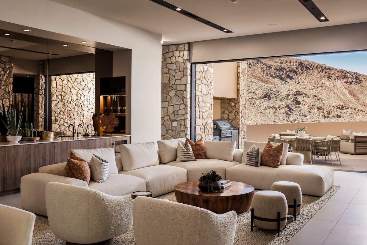 Modern open-concept living room with plush sectional sofa, stone accent walls, indoor-outdoor flow, and luxury desert mountain views.