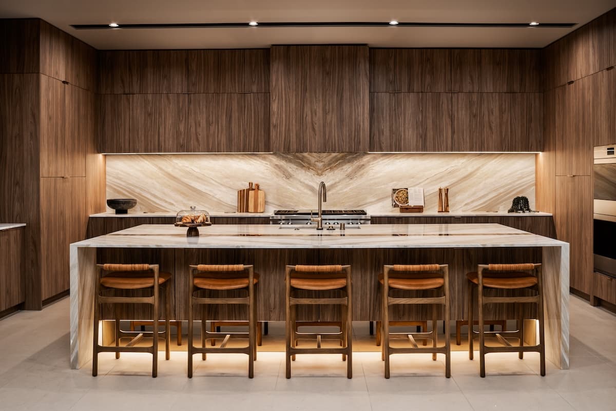 Modern luxury kitchen with dark wood cabinetry, marble waterfall island, bar seating, and high-end appliances.