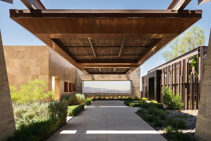Ascaya clubhouse entrance with modern architectural design, featuring a shaded breezeway, desert landscaping, and a framed view of the Las Vegas Strip in the distance.