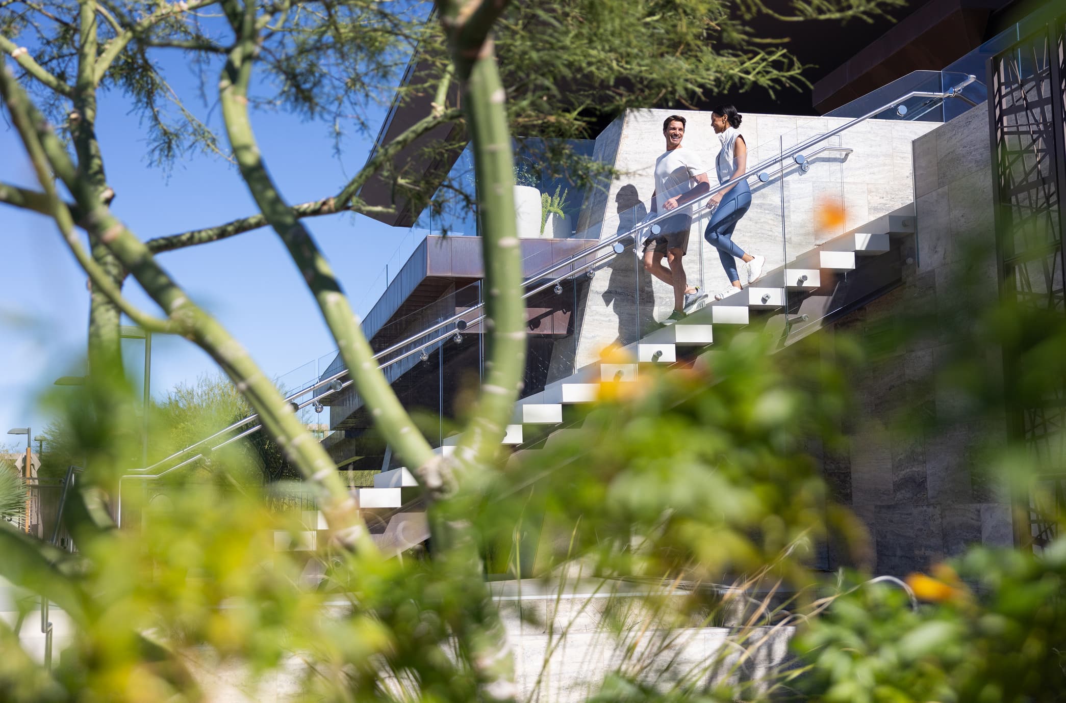 Couple walking down modern outdoor stairs beside a contemporary home framed by desert landscaping.