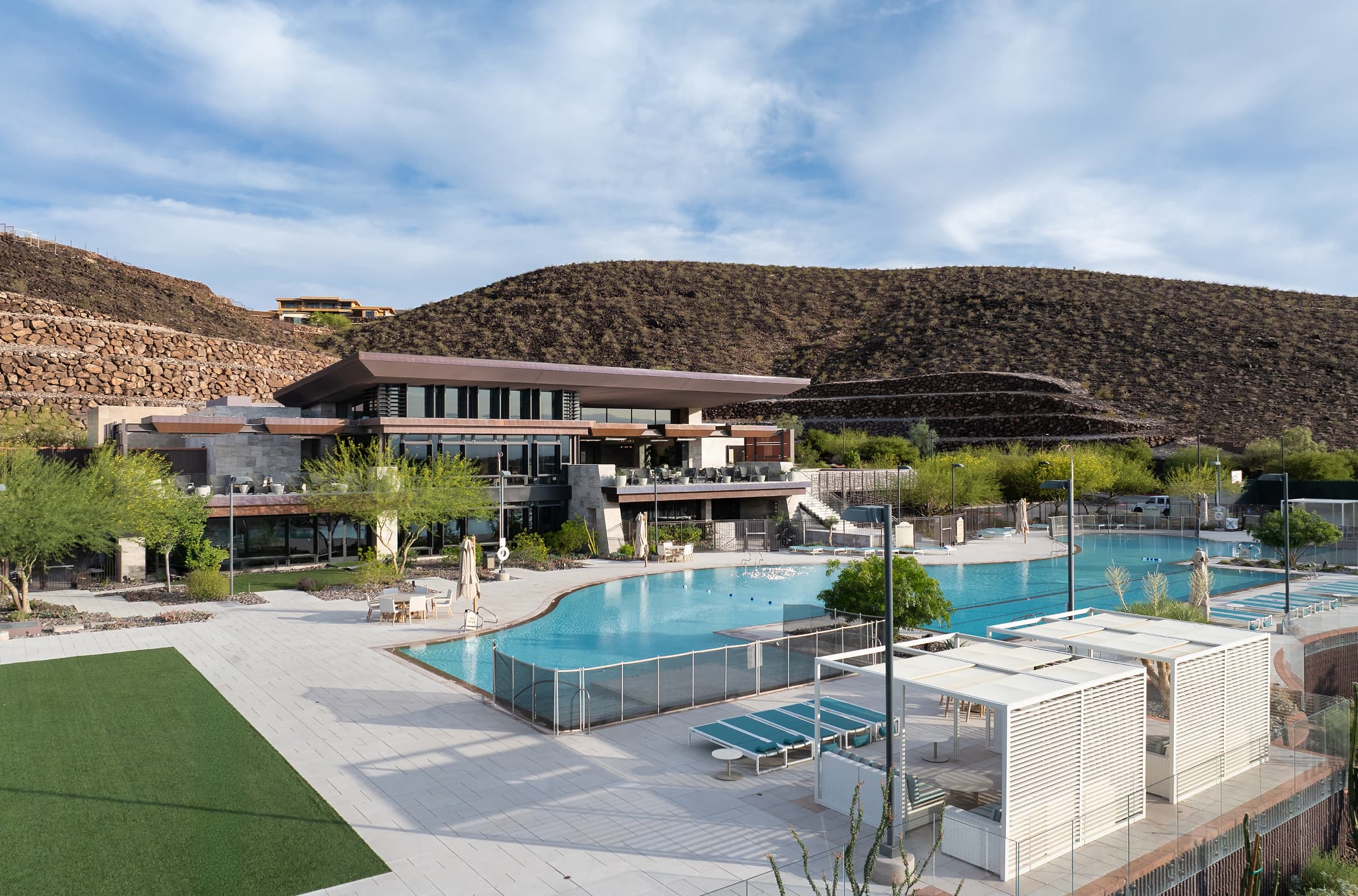 Modern clubhouse and pool area set against desert hills with lounge seating and landscaped grounds.