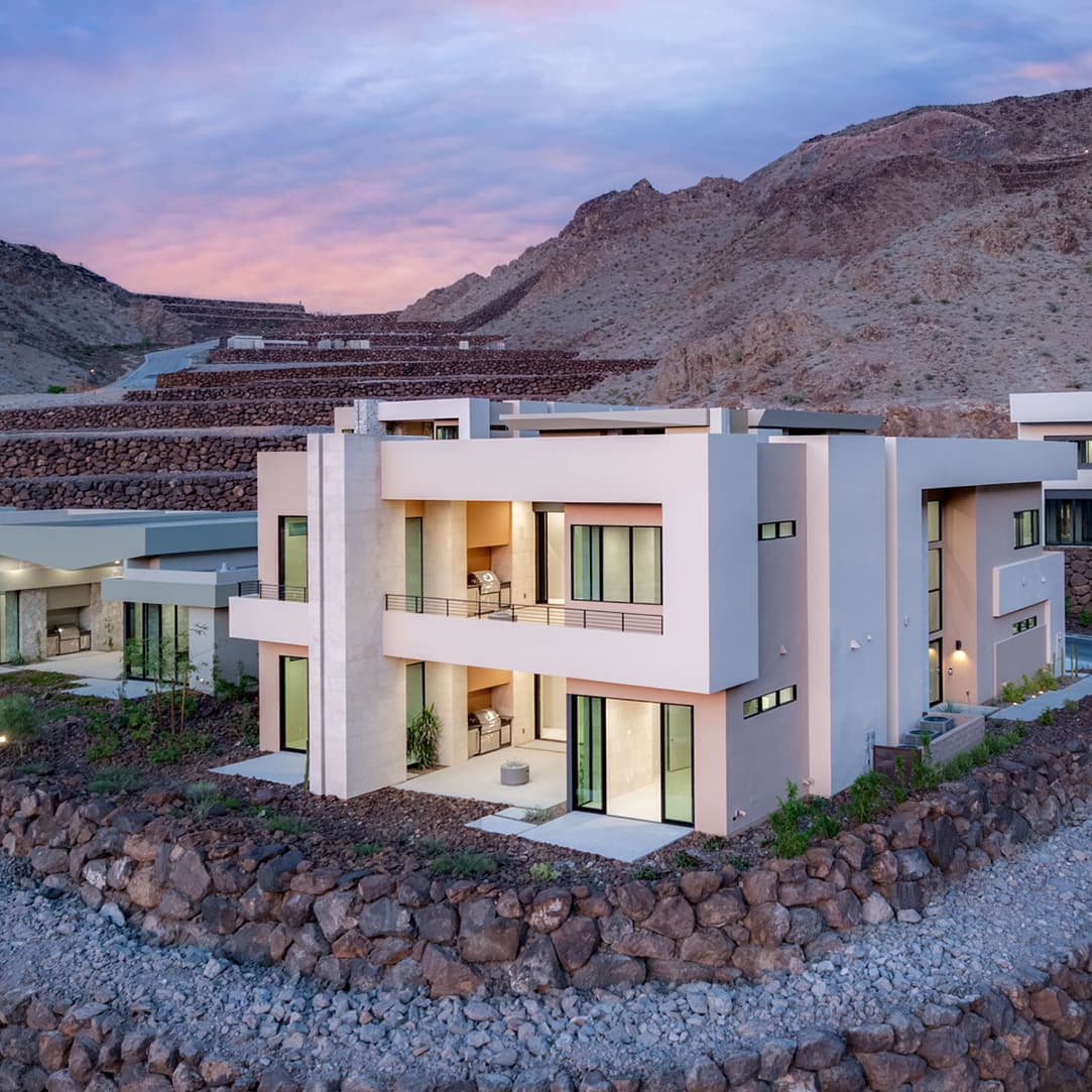Modern canyon-side residence with expansive balconies, floor-to-ceiling windows, and contemporary desert architecture set against terraced mountain landscapes at dusk