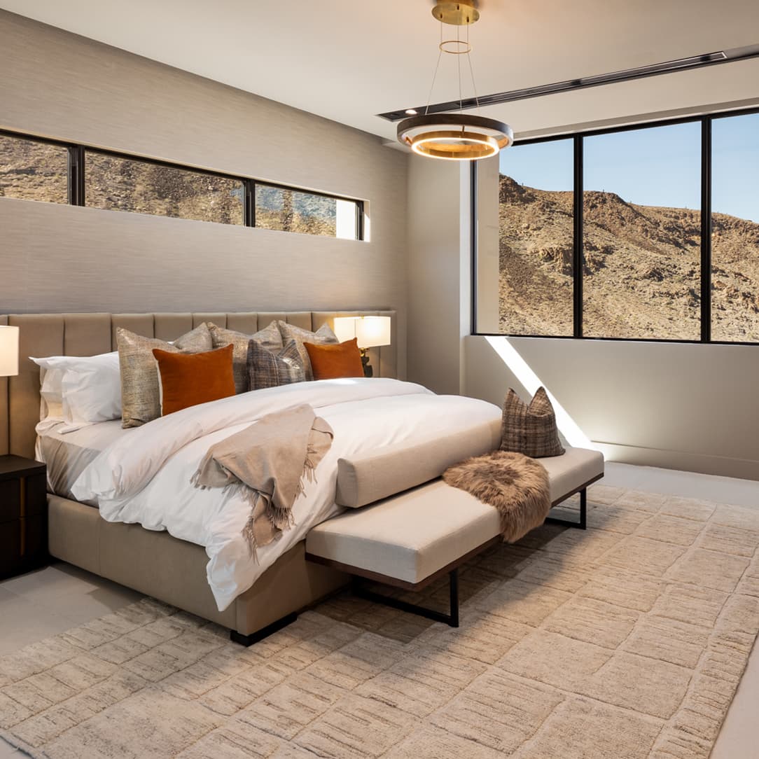 Contemporary bedroom suite with plush upholstered furnishings, warm modern lighting, and expansive windows overlooking rugged desert mountain views