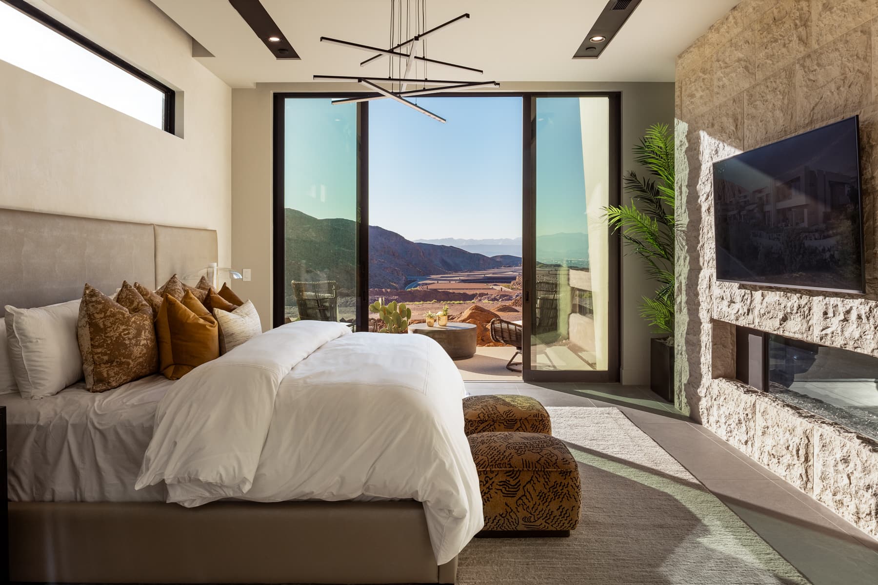 Luxury primary bedroom with floor-to-ceiling glass doors, modern linear fireplace, private terrace, and panoramic desert mountain views