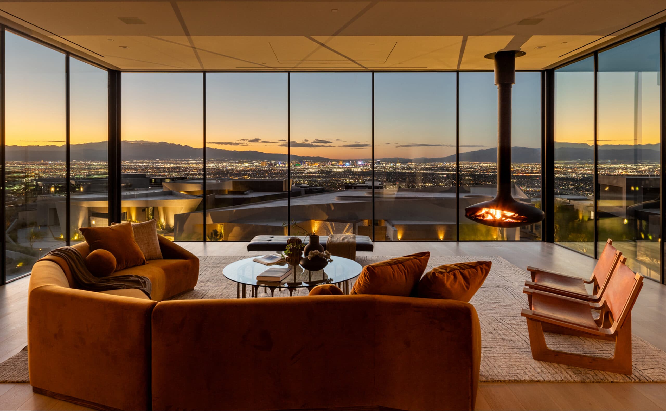 Luxury modern living room with panoramic floor-to-ceiling windows, fireplace, and stunning Las Vegas skyline at sunset.
