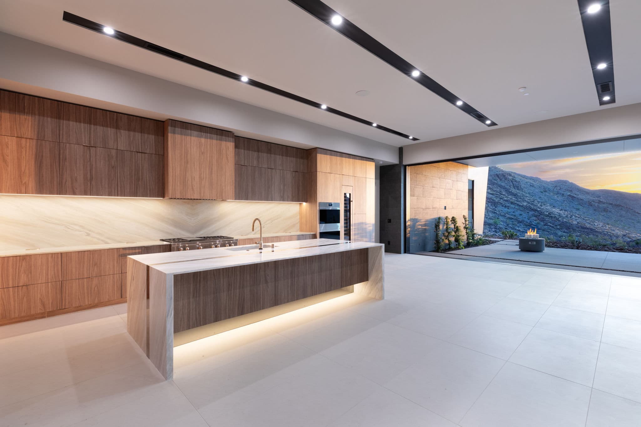 Luxury kitchen with illuminated waterfall island, custom cabinetry, and expansive indoor-outdoor living design”