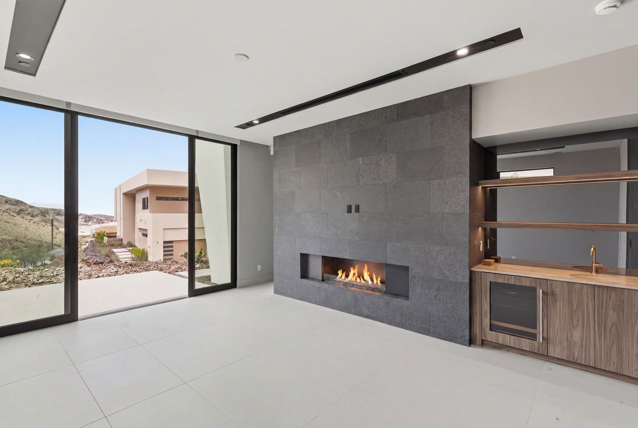 Modern indoor-outdoor living space with linear fireplace, built-in wet bar, and sliding glass doors opening to a private desert patio