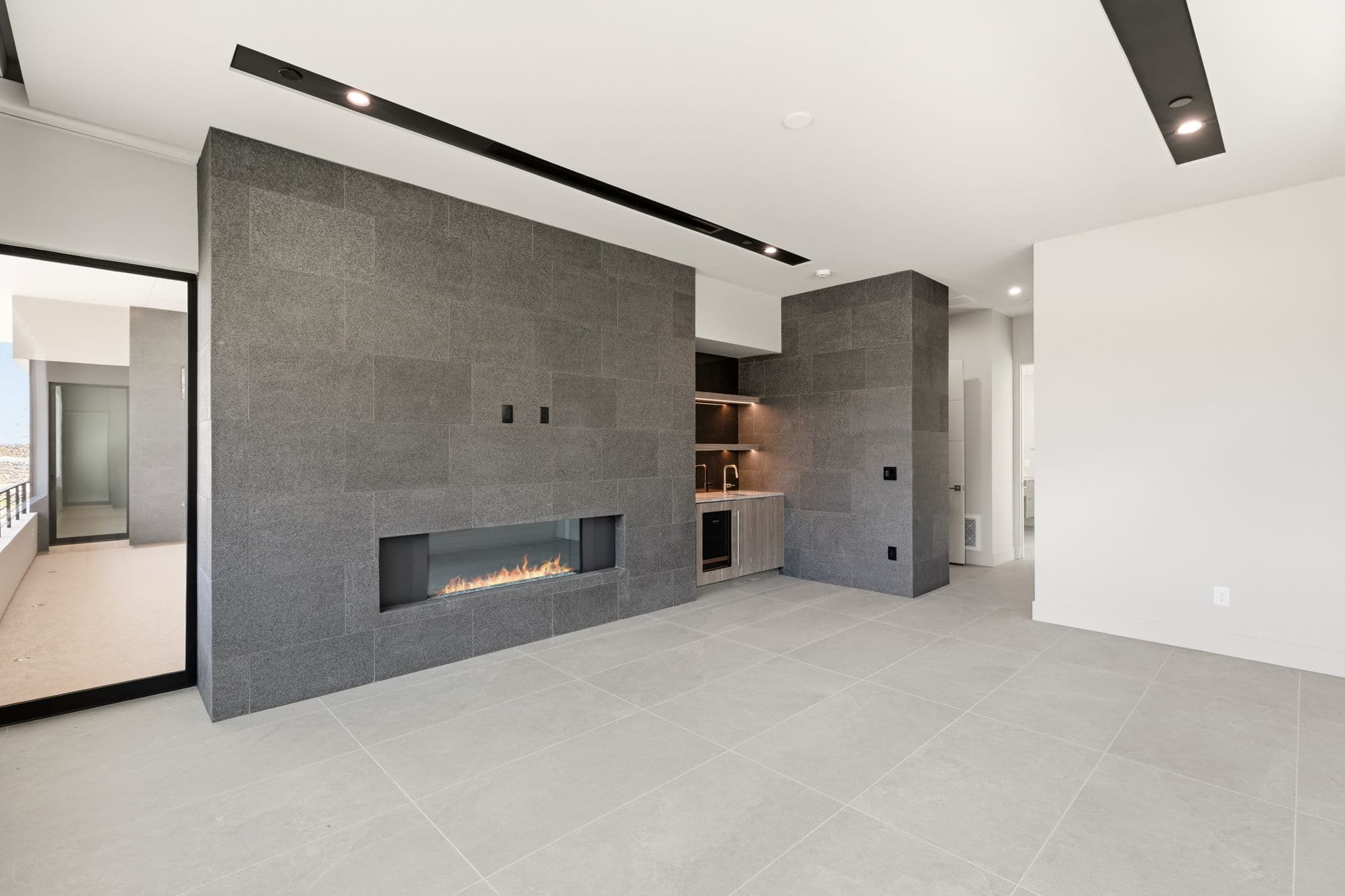 Contemporary lounge with floor-to-ceiling charcoal stone fireplace, built-in wet bar, recessed lighting, and expansive open-concept design