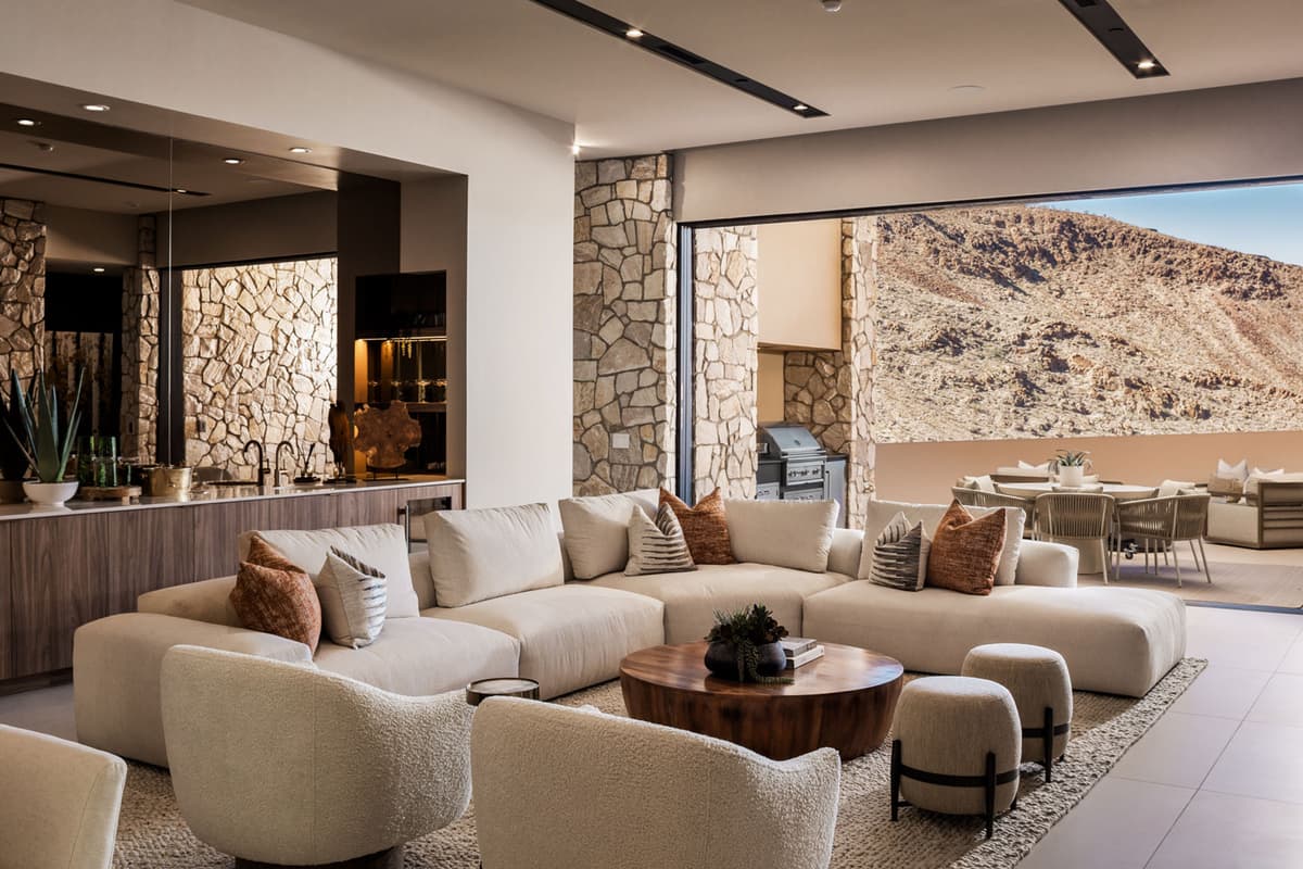 Modern open-concept living room with plush sectional sofa, stone accent walls, indoor-outdoor flow, and luxury desert mountain views.
