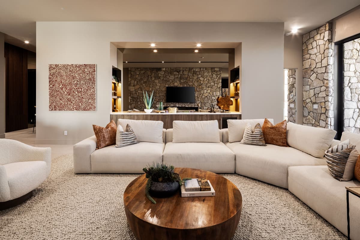 Modern open-concept living room with plush sectional sofa, stone accent walls, indoor-outdoor flow, and luxury desert mountain views.
