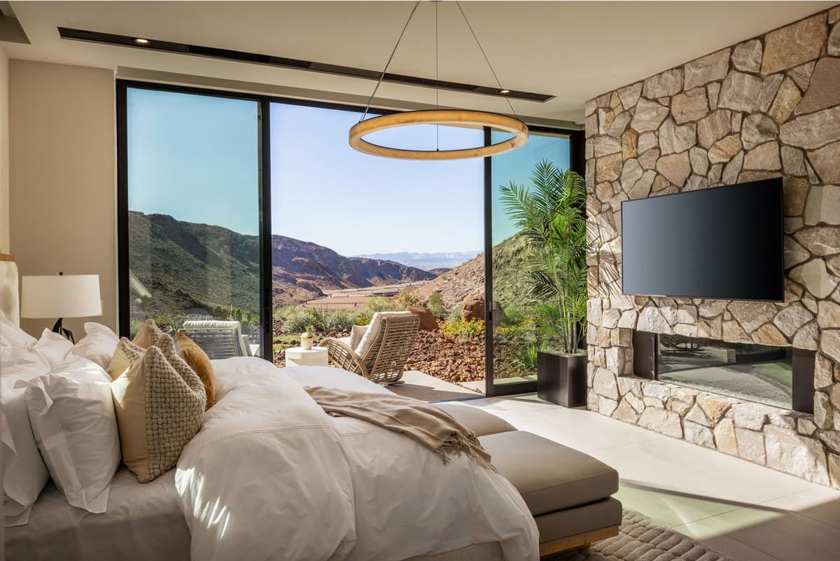 Modern luxury bedroom with stone fireplace, large glass doors, and scenic desert mountain views.