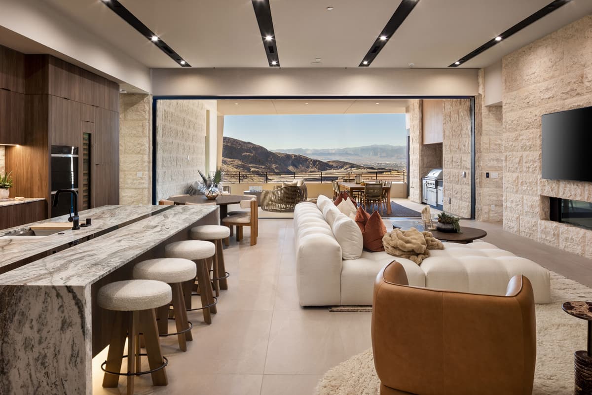 Luxury open-concept kitchen and living room with marble island, modern seating, and expansive indoor-outdoor desert mountain views.