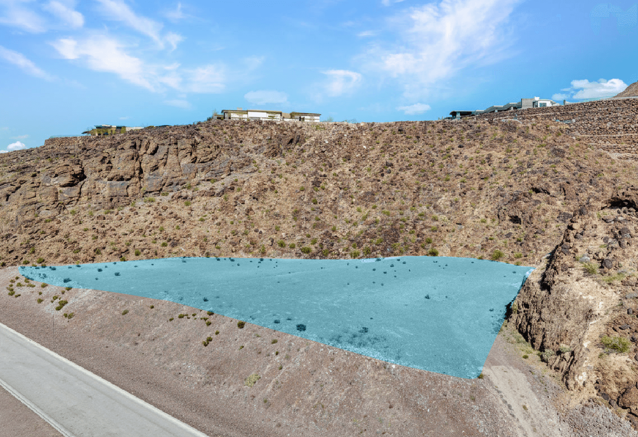 Aerial view of Ascaya Homesites 57 and 58, outlined in blue beneath a dramatic rocky mountainside with neighboring modern homes above.