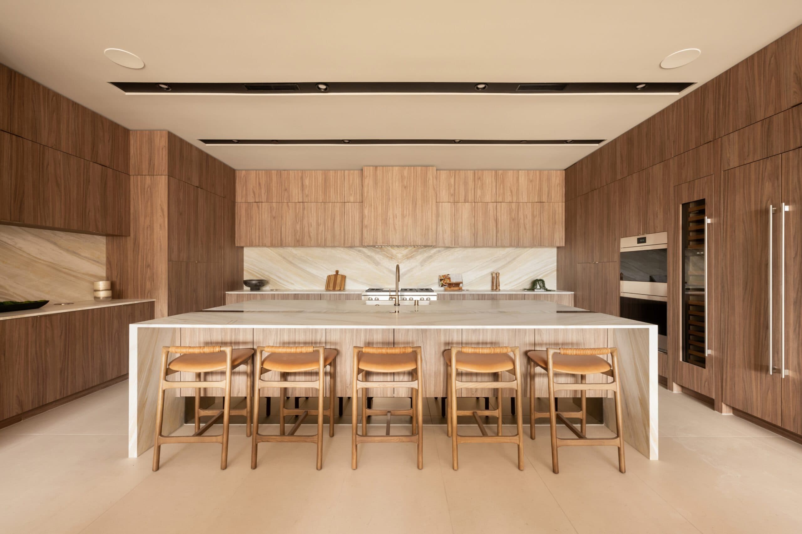 Luxury modern kitchen with rich wood cabinetry, marble surfaces, a spacious island, and elegant bar seating.