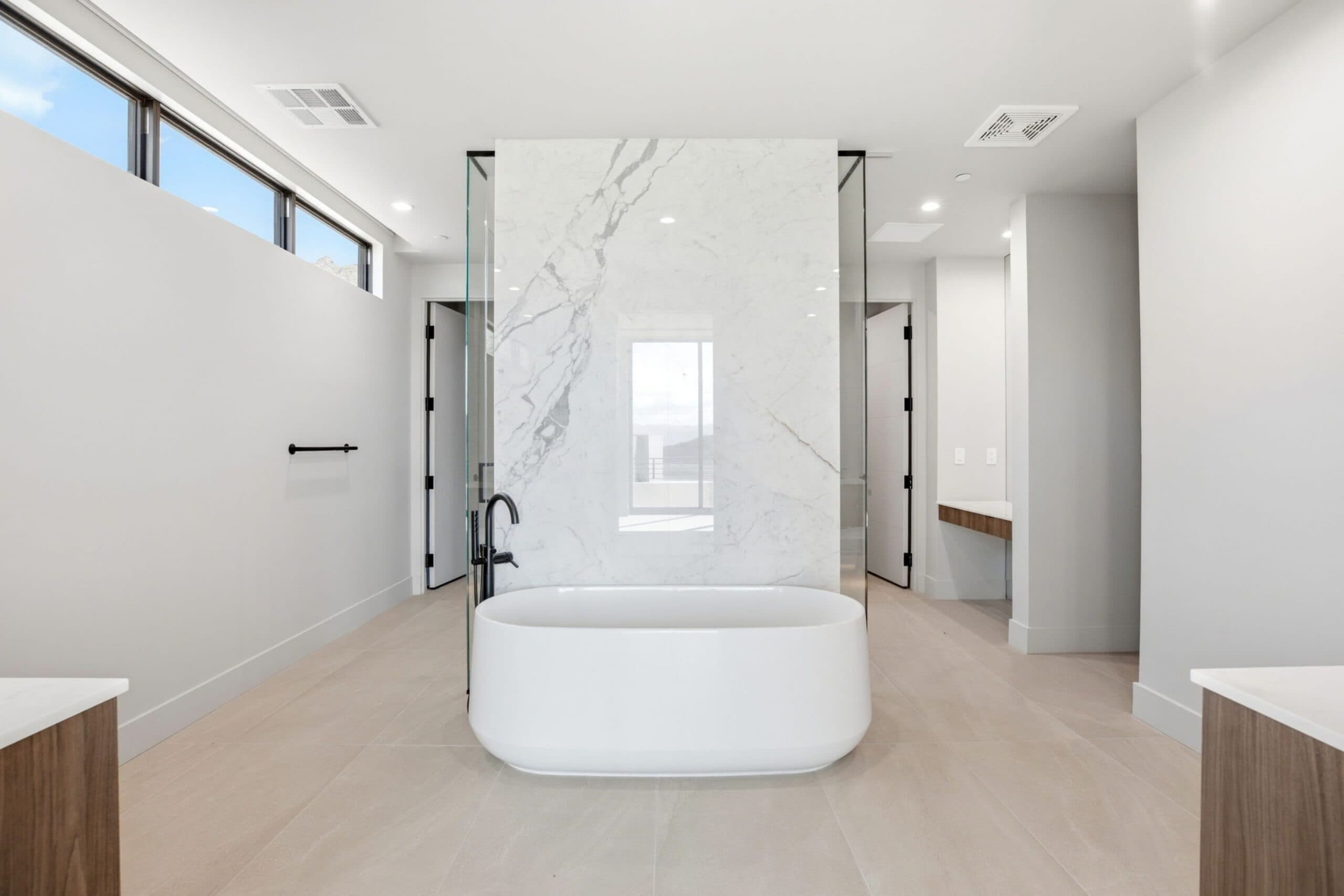 Modern luxury bathroom with a freestanding soaking tub, dramatic marble feature wall, glass shower, and minimalist finishes.