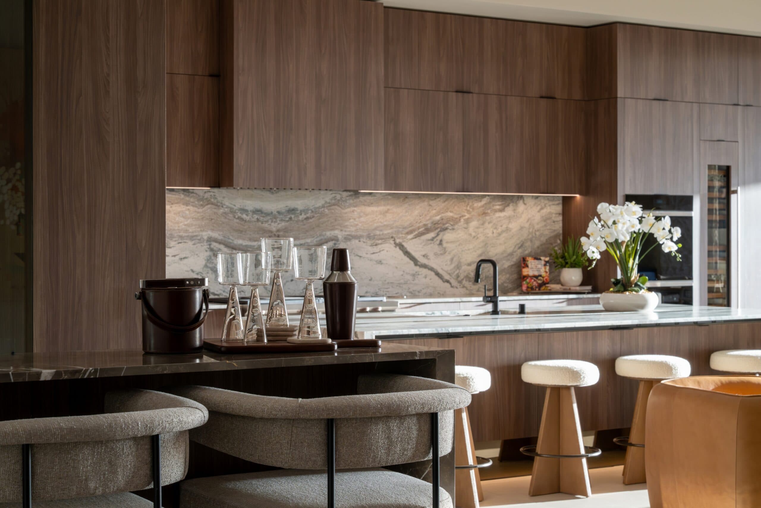 Luxury modern kitchen and dining space with rich wood cabinetry, marble surfaces, stylish seating, and elegant contemporary finishes.