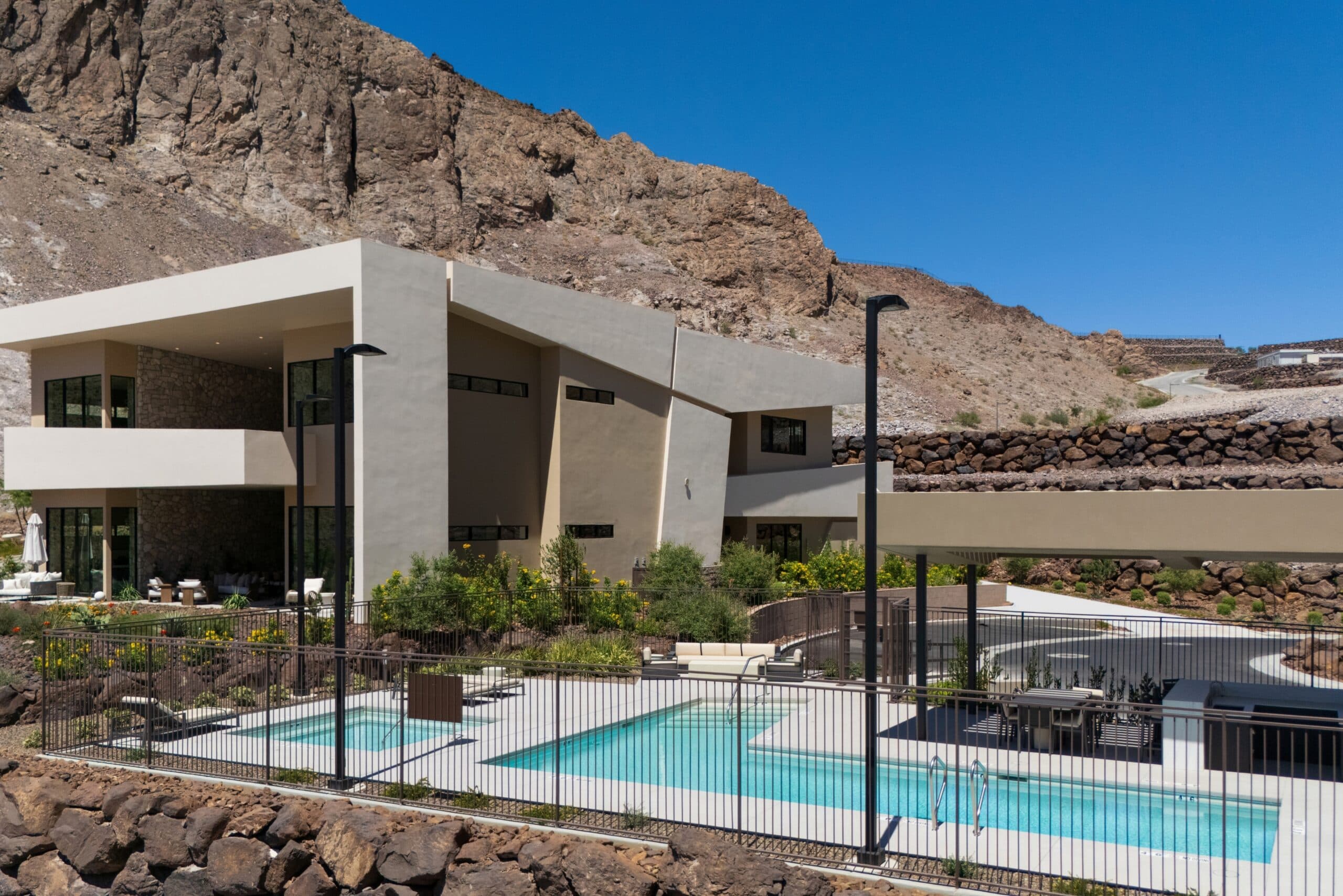 Modern luxury desert residence with geometric architecture, landscaped outdoor spaces, and a private swimming pool set against rugged mountain cliffs.