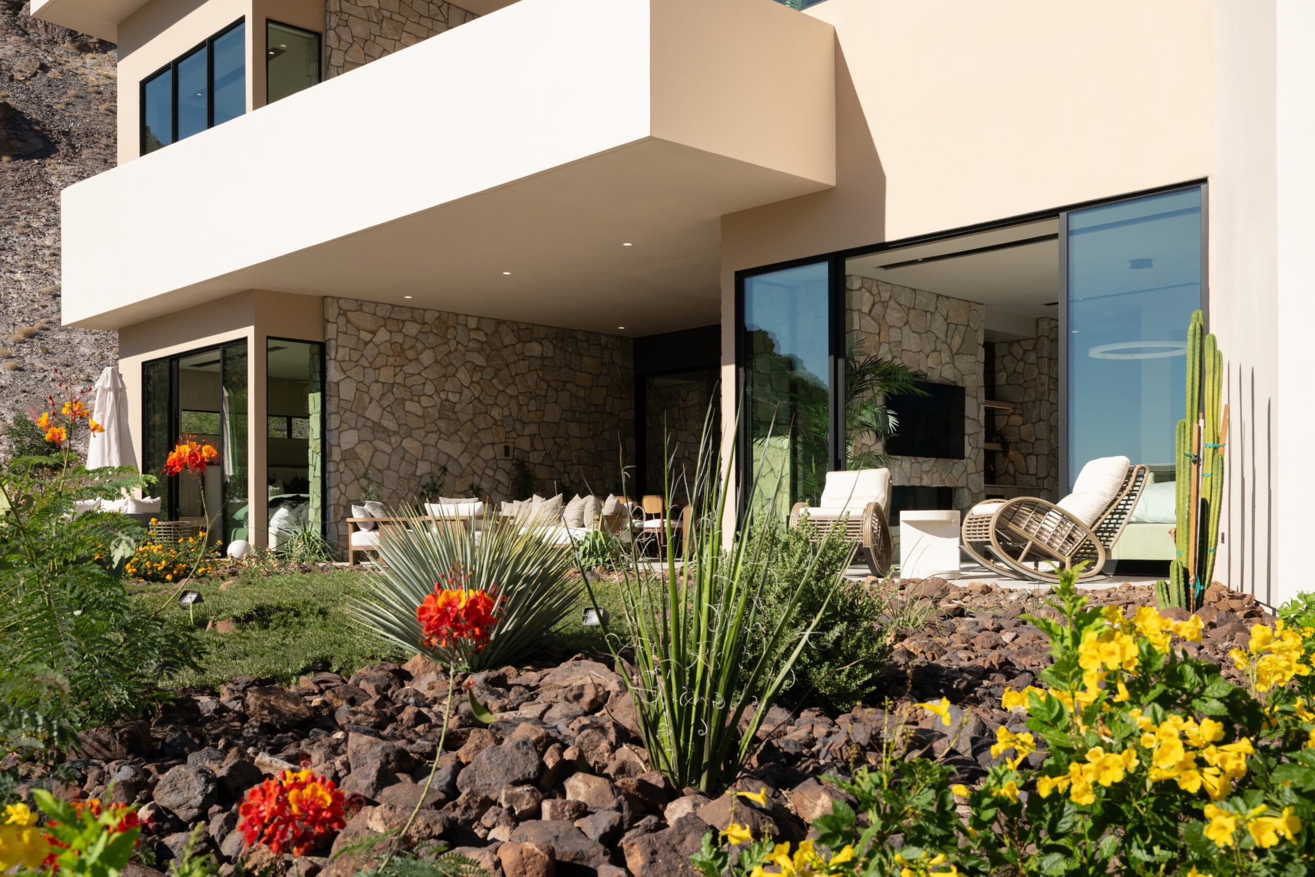 Modern luxury desert home with stone accents, floor-to-ceiling windows, and vibrant drought-tolerant landscaping.