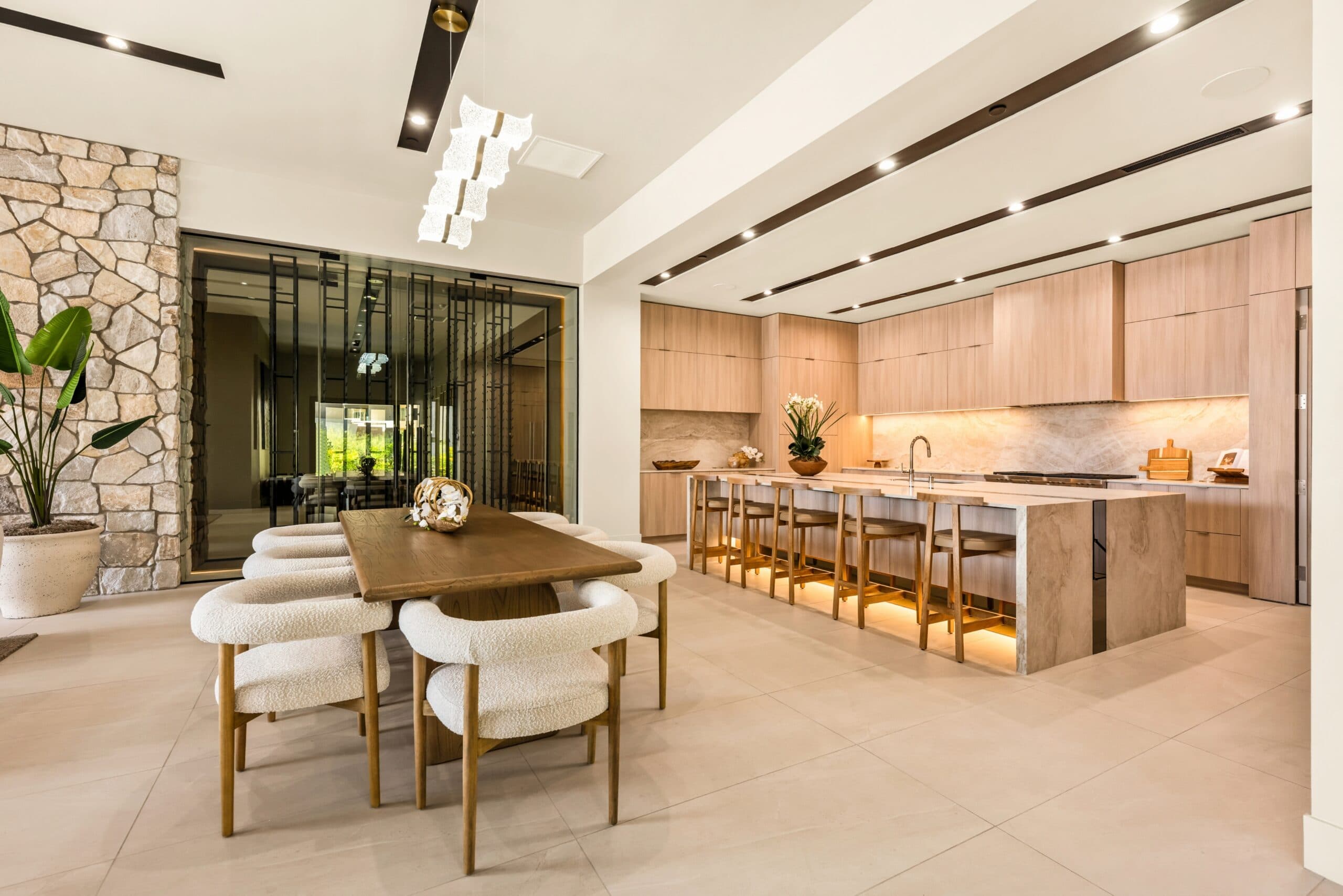 Luxury open-concept kitchen and dining area with warm wood cabinetry, stone finishes, a large island, and contemporary lighting.