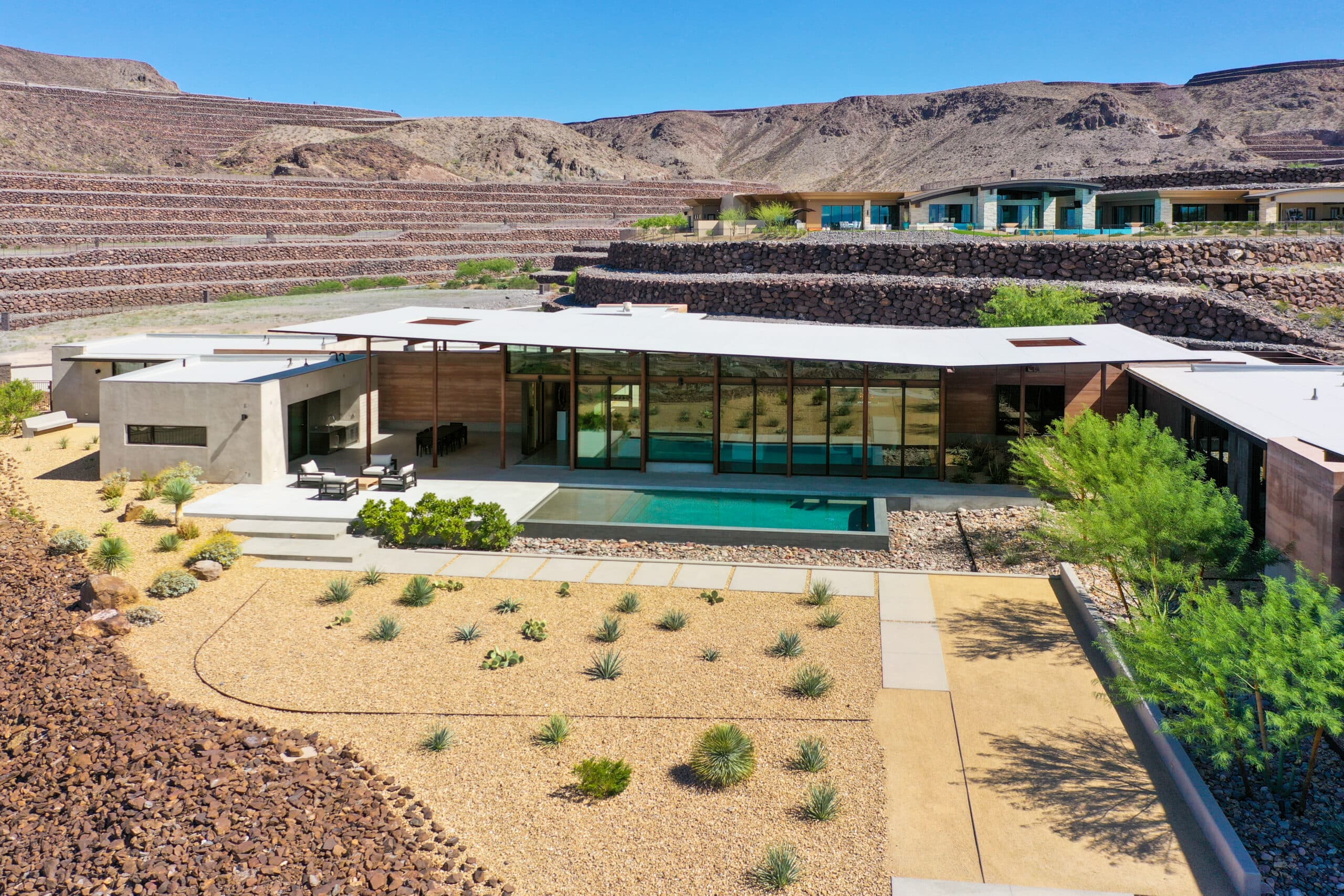 Modern single-story desert residence with expansive glass walls, a linear pool, and minimalist landscaping, set into Ascaya’s terraced hillside with sweeping mountain surroundings.