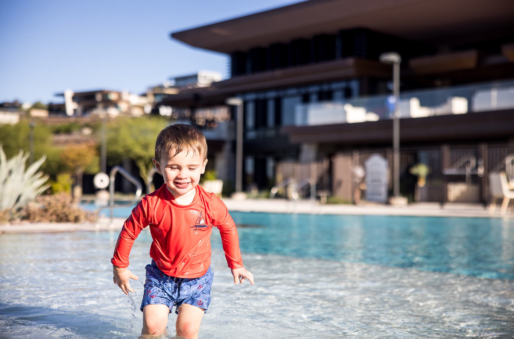 A child playing in a shallow splash pad, enjoying a family-friendly water feature with gentle fountains and a resort-style pool setting nearby.