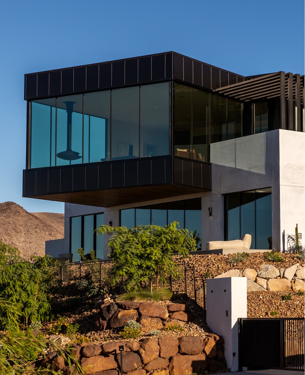 Modern luxury glass home with floor-to-ceiling windows, cantilever design, and desert mountain views.