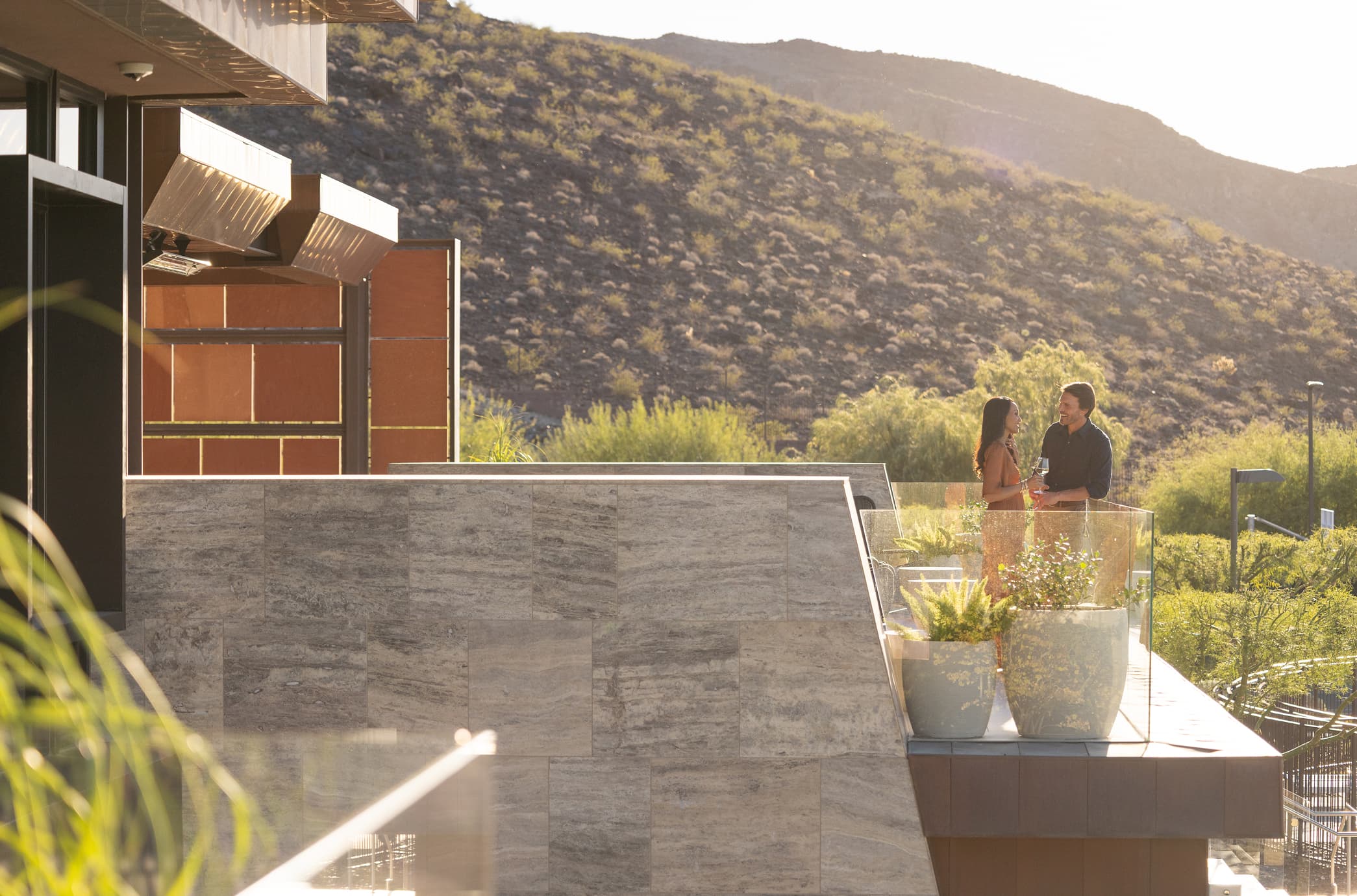 Couple enjoying drinks on a luxury rooftop terrace with desert mountain views at sunset.