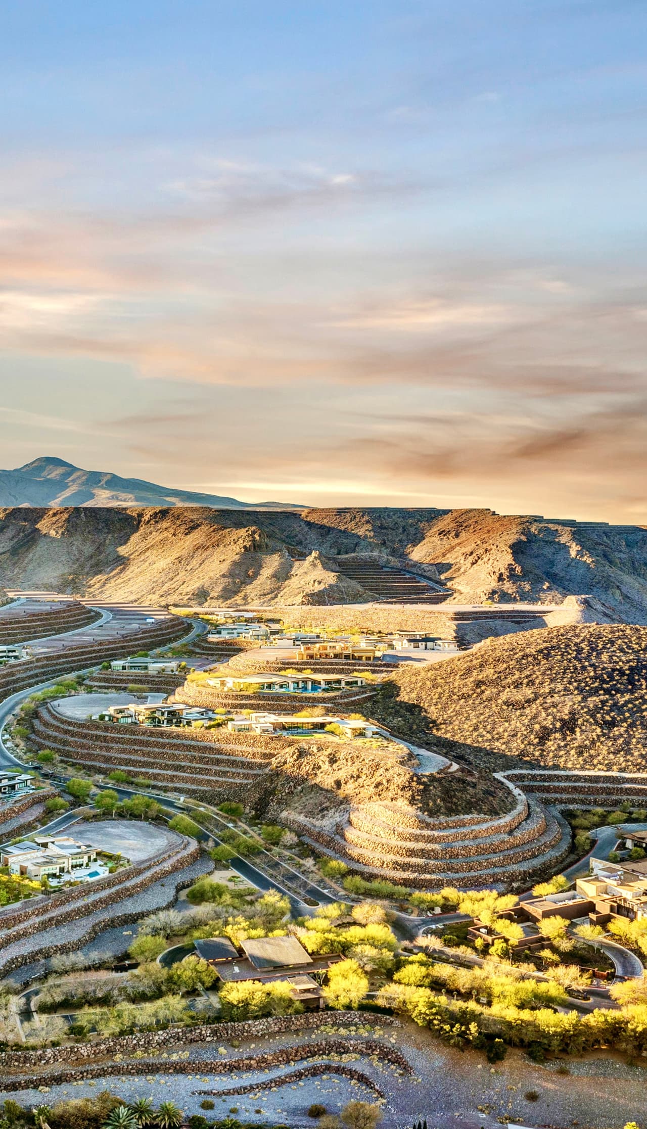 Aerial view of a terraced desert landscape with winding roads and modern homes at sunset.