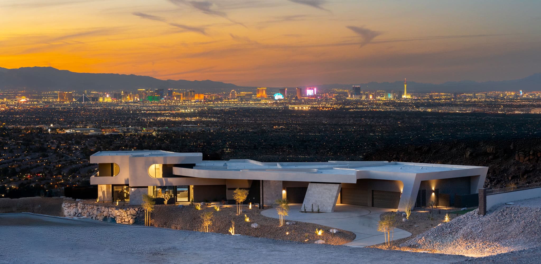 Modern luxury hillside home overlooking Las Vegas Strip skyline at sunset with city lights.