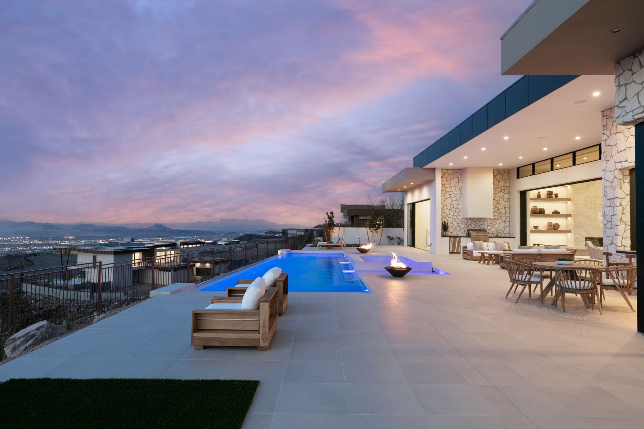 Luxury outdoor living terrace in Ascaya with infinity-edge pool, fire features, and panoramic Las Vegas valley views at sunse