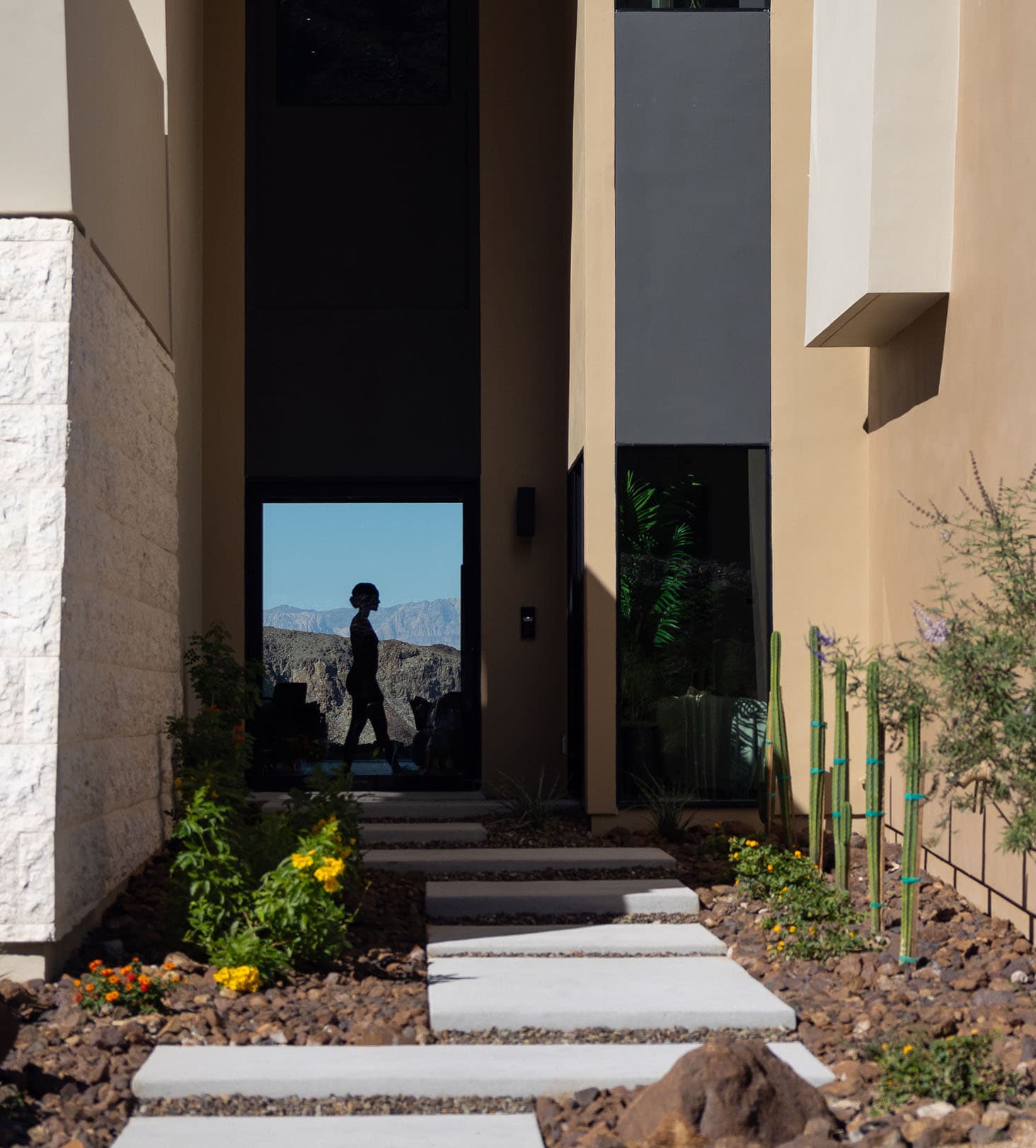 Modern luxury home entrance with desert landscaping, stone pathway, and glass doorway with mountain views.