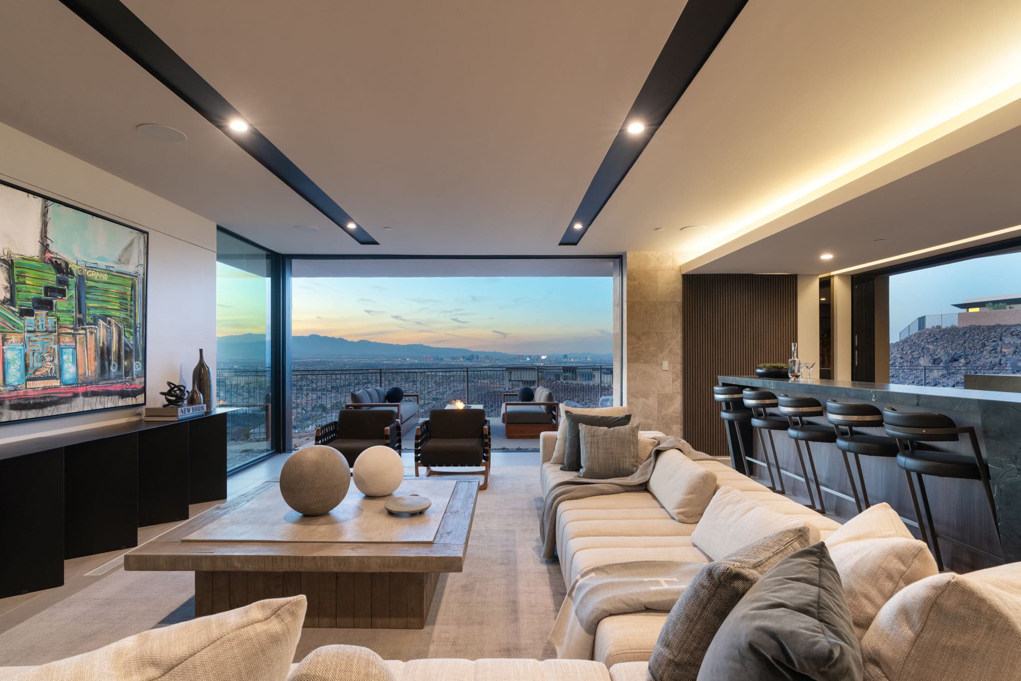 Sophisticated modern great room with expansive floor-to-ceiling pocket doors, panoramic Las Vegas Strip views, a sleek entertainment bar, and warm contemporary furnishings designed for seamless indoor-outdoor luxury living.