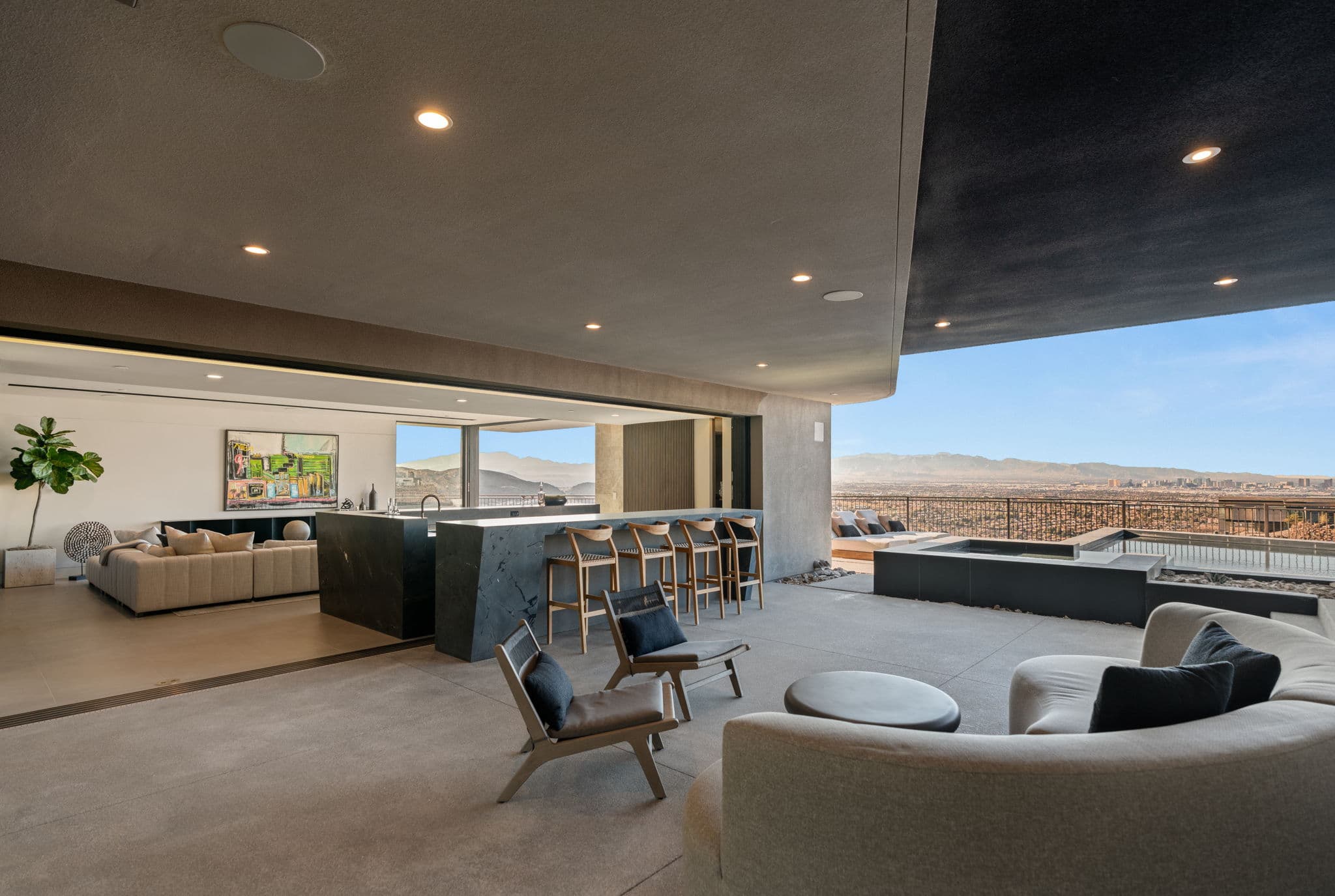 Expansive covered outdoor living space featuring a sculptural entertainment bar, integrated fire feature, panoramic Las Vegas skyline views, and seamless indoor-outdoor flow designed for elevated desert luxury living.