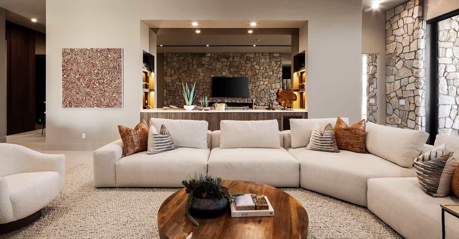 Luxury open-concept living room with curved sectional sofa, stone feature wall, built-in bar, and modern desert home design.