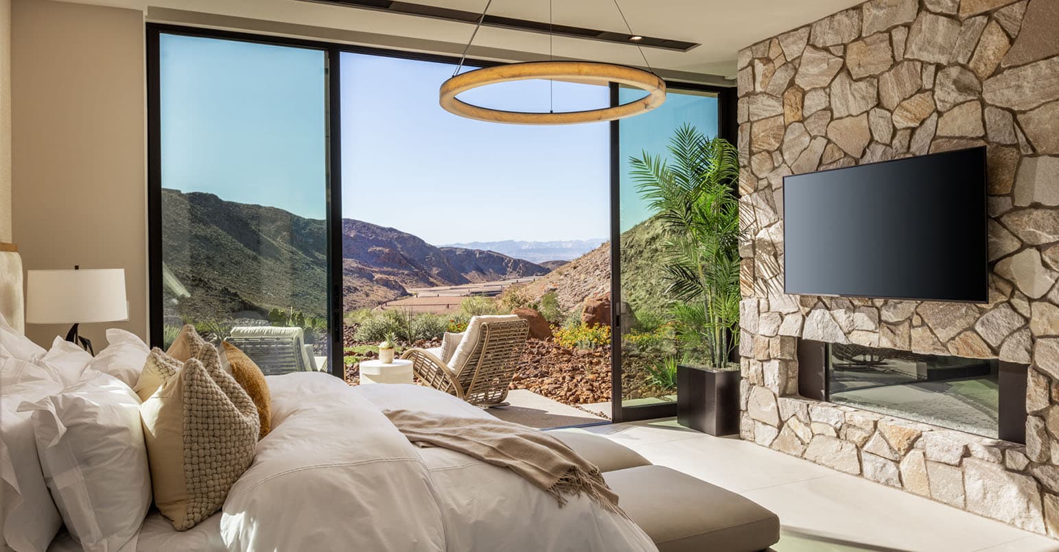 Modern luxury bedroom with stone fireplace, large glass doors, and scenic desert mountain views.