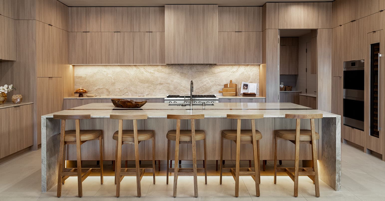 Modern luxury kitchen with wood cabinetry, marble island, bar stools, and built-in appliances.