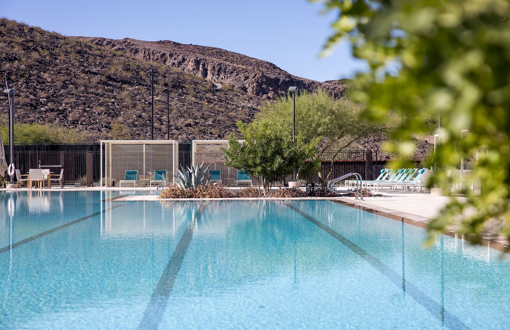 A serene zero-edge pool set against the rugged desert landscape, with crystal-clear water, private cabanas, and lounge seating framed by native greenery and mountain views.