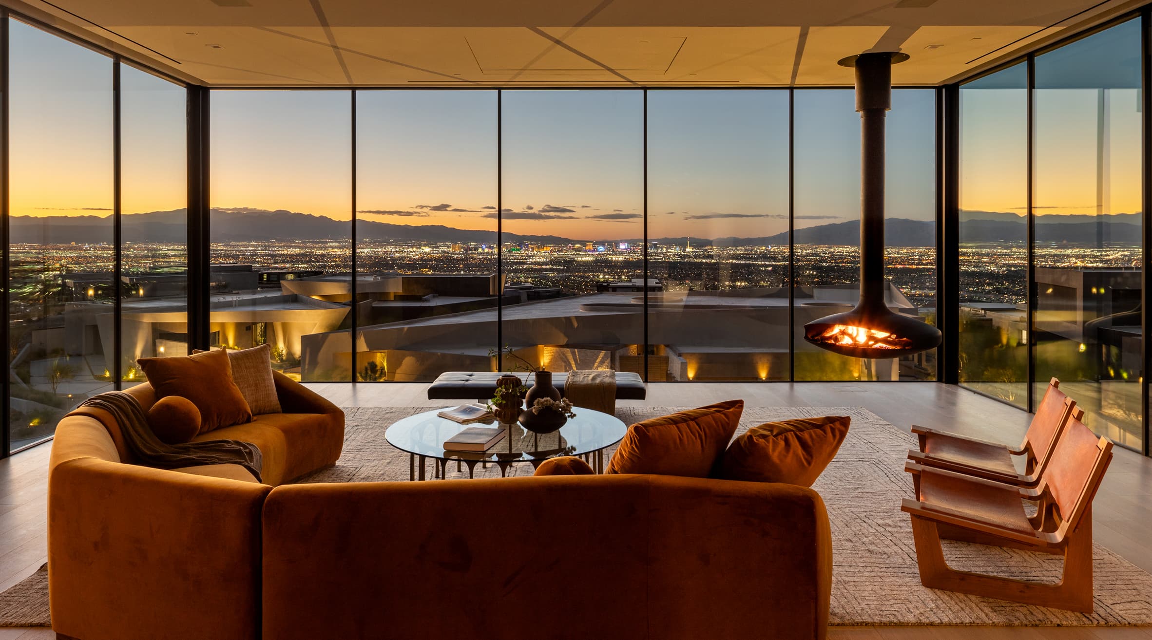 Luxury modern living room with panoramic floor-to-ceiling windows, fireplace, and stunning Las Vegas skyline at sunset.