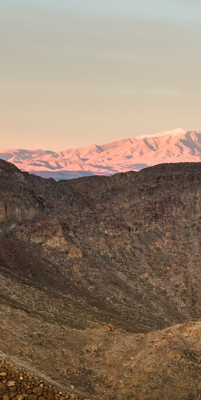 Desert landscape with rocky terrain and distant sand dunes glowing at sunset.