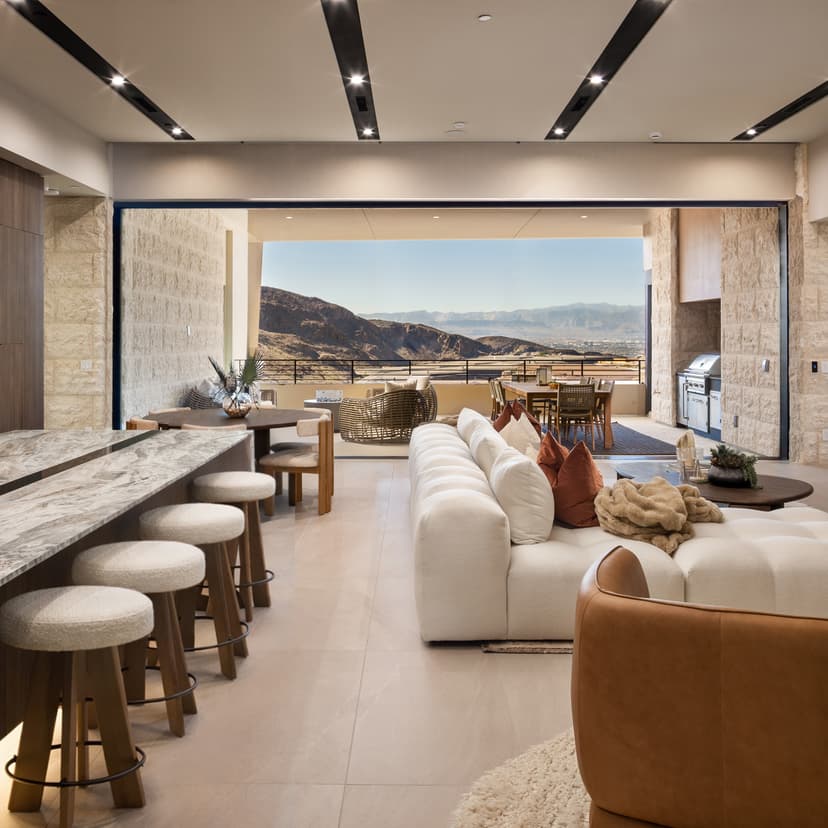 Luxury open-concept kitchen and living room with marble island, modern seating, and expansive indoor-outdoor desert mountain views.