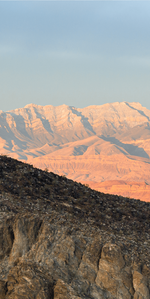 Expansive desert mountain landscape near Ascaya, showcasing layered ridgelines and warm, sunlit tones against a clear sky.